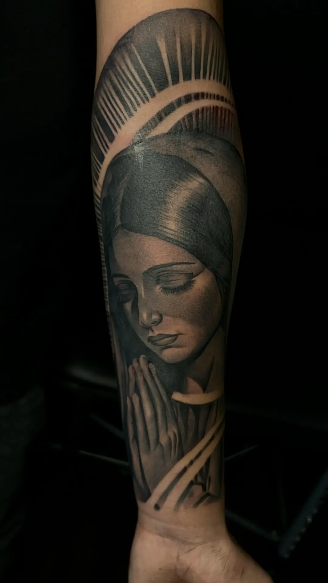 Black and grey realism portrait of a woman with praying hands on a forearm