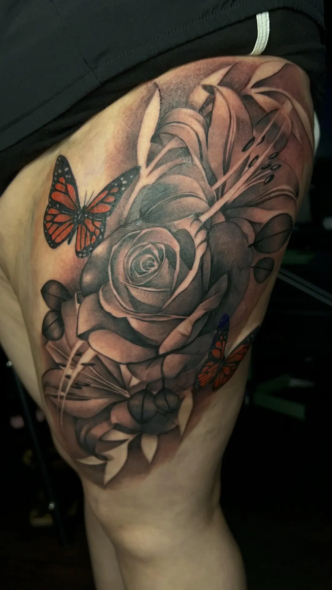 Shaded rose tattoo with orange and black butterflies on an upper arm
